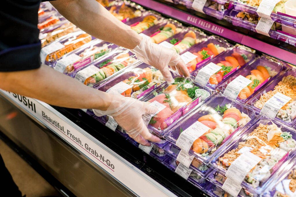 A man placing packaged sushi on a supermarket shelf